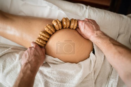Photo for Unknown Caucasian woman having madero therapy massage anti-cellulite treatment by professional therapist holding wooden tools in hands in studio or salon with copy space - Royalty Free Image