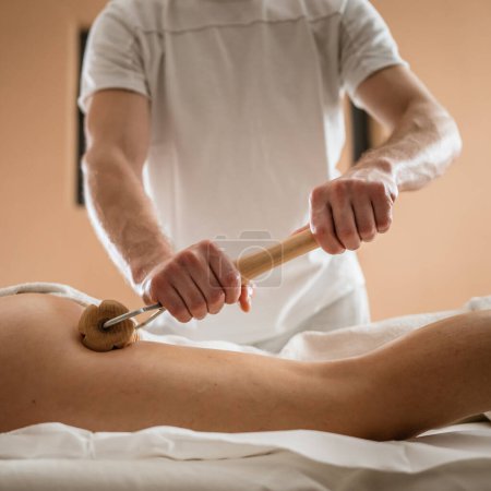 Téléchargez les photos : Femme caucasienne inconnue ayant madero thérapie massage traitement anti-cellulite par un thérapeute professionnel tenant des outils en bois dans les mains en studio ou salon avec espace de copie - en image libre de droit