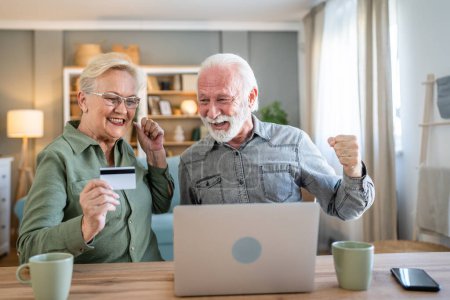 Photo for Couple mature senior women and man husband and wife sit at home use credit or debit card for online shopping browse internet stores buying stuff use laptop computer real people copy space - Royalty Free Image