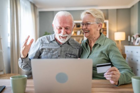 Photo for Couple mature senior women and man husband and wife sit at home use credit or debit card for online shopping browse internet stores buying stuff use laptop computer real people copy space - Royalty Free Image