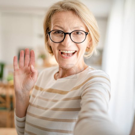 Photo for Portrait of one mature blonde caucasian woman with eyeglasses at home happy smile looking to the camera confident wear sweater in bright room user generated content self portrait selfie ugc copy space - Royalty Free Image