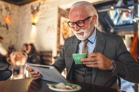 Téléchargez les photos : Un homme haut caucasien homme d'affaires homme d'affaires propriétaire d'utiliser une tablette numérique assis au café costume espace de copie de vêtements ont tasse de café - en image libre de droit