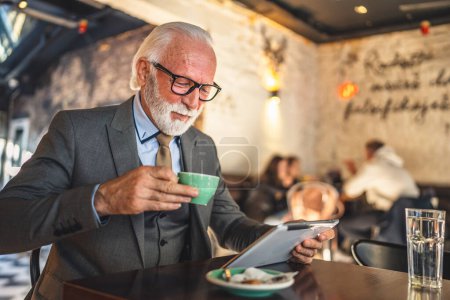 Foto de Un hombre mayor caucásico hombre de negocios hombre de negocios uso tableta digital sentarse en la cafetería desgaste traje copia espacio tienen taza de café - Imagen libre de derechos