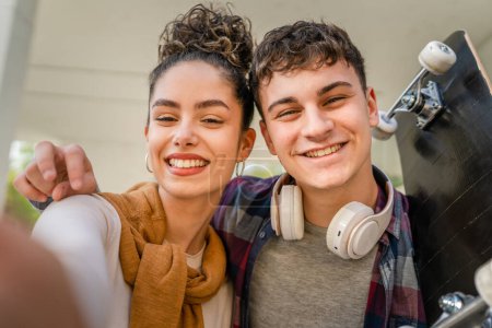 Photo for Young man and woman teenager couple caucasian brother and sister take selfies self portrait by modern building in day happy smile carry skateboard real people family love concept copy space - Royalty Free Image