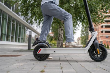 Téléchargez les photos : Pieds de femme inconnue debout ou conduire scooter électrique coup de pied e-scooter sur le trottoir dans le transport moderne respectueux de l'environnement de jour dans la ville ou la ville - en image libre de droit