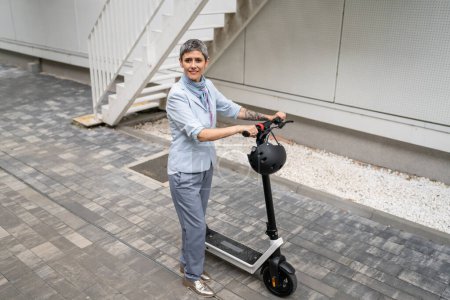 Téléchargez les photos : Une femme mature caucasienne senior debout en plein air avec scooter électrique coup de pied dans la journée confiante femme d'affaires en utilisant un mode de transport alternatif personnes réelles copier l'espace - en image libre de droit