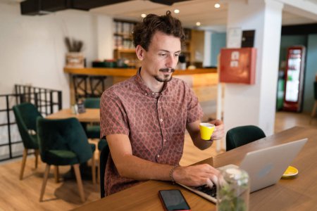 Photo for One adult modern man caucasian male with beard and mustaches wear causal shirt working remote from cafe freelance work or blog checking online content or browsing internet while sitting alone - Royalty Free Image