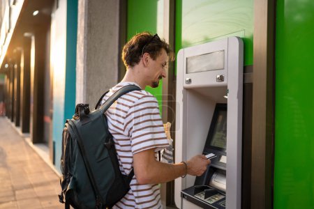 Photo for One man young adult modern millennial tourist using atm machine to withdraw money urban life modern living concept side view male hold card copy space - Royalty Free Image