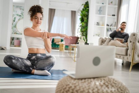 Foto de Una mujer joven caucásica yoga femenino estiramiento práctica en casa en línea a través de ordenador portátil instrucciones de Internet coursev - Imagen libre de derechos