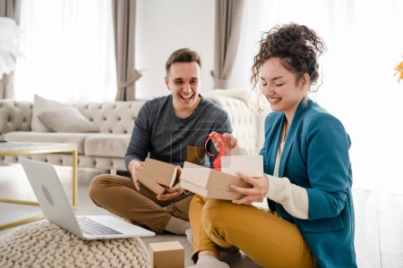 Photo for Young couple man and woman boyfriend and girlfriend or husband and wife exchange gifts at home giving presents to each other and opening box happy smile celebrate valentine holiday or birthday - Royalty Free Image