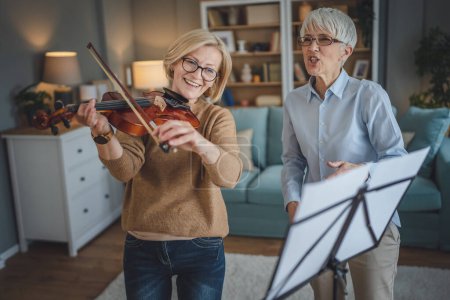 Photo for Two women mature female teacher give private violin lesson to her student or friend at home help her to learn to play in room hobby and leisure active senior concept copy space - Royalty Free Image