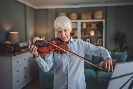 Téléchargez les photos : Mature femme caucasienne senior apprendre à jouer du violon pratique à la maison - en image libre de droit