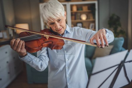 Photo for Mature senior caucasian woman learn to play violin practice at home - Royalty Free Image