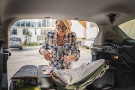 Photo for One mature blonde beautiful woman travel concept female take stuff belongings from the back of her car while moving or arrive to destination real people copy space - Royalty Free Image