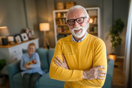 Téléchargez les photos : Portrait d'un homme âgé avec barbe et cheveux gris porter des lunettes heureux sourire positive émotion copie espace debout à la maison intérieur pull jaune - en image libre de droit