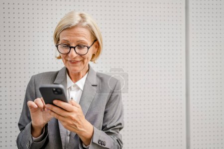 Téléchargez les photos : Une femme mature caucasienne blonde femme utiliser téléphone mobile smartphone pour envoyer des messages texte sms seul heureux confiant vraies personnes copier l'espace - en image libre de droit