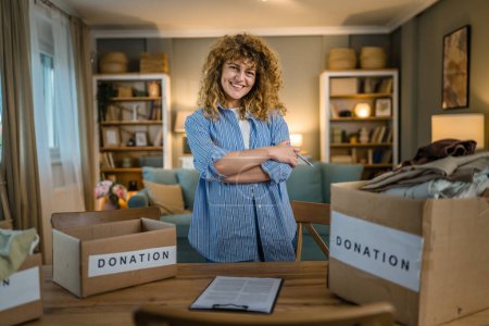 Photo for One young adult woman caucasian female with curly hair prepare wardrobe clothes for charity donation help at home stand in front of stuff in the boxes confident portrait - Royalty Free Image