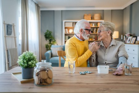 Téléchargez les photos : Couple âgé femme vérifier mesurer la pression artérielle tandis que son mari vieil homme caucasien assis à côté de la table à la maison de vraies personnes famille personnes âgées retraite et concept de santé - en image libre de droit