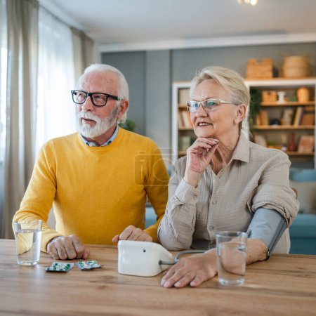 Photo for Senior couple woman check measure blood pressure while her husband old caucasian man sit beside at the table at home real people family old people retirement and health concept - Royalty Free Image