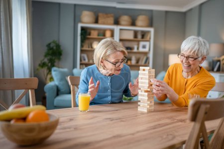 Photo for Two senior women female woman friends or family sisters play leisure board game at home have fun pensioner grandmother spend time together with their mature daughter - Royalty Free Image