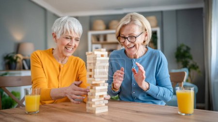 Photo for Two senior women female woman friends or family sisters play leisure board game at home have fun pensioner grandmother spend time together with their mature daughter - Royalty Free Image