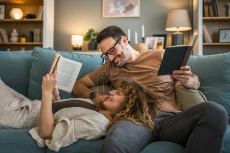 Photo for Adult couple man and woman Caucasian husband and wife in a relationship real book hold books on the sofa bed at home in the apartment reading leisure bonding family concept real people copy space - Royalty Free Image