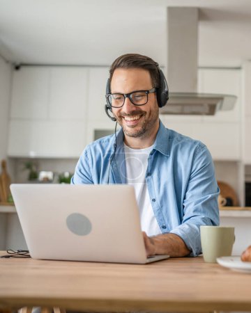 Photo for One man caucasian male freelancer work from home with headphones on his head on laptop computer customer support happy smile confident - Royalty Free Image