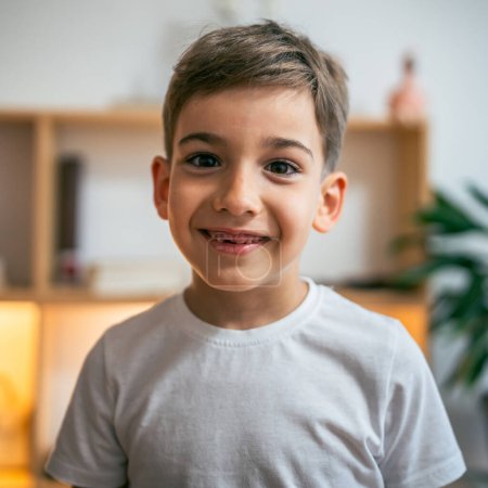 Téléchargez les photos : Portrait de heureux enfant d'âge préscolaire caucasien Garçon sans lait dent supérieure en blanc t-shirt sourire avec trou dans la bouche stand à la maison espace de copie - en image libre de droit