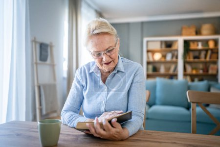 Téléchargez les photos : Une femme mature caucasienne âgée retraité grand-mère moderne lire le livre à la maison porter des lunettes espace de copie personne réelle - en image libre de droit