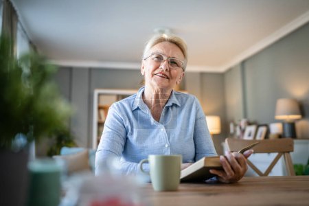 Photo for One woman mature senior caucasian female pensioner modern grandmother read book at home wear eyeglasses real person copy space - Royalty Free Image