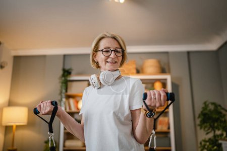 Photo for One woman mature blonde female training at home in room using rubber resistance bands tubes sportswoman doing exercises alone health and fitness concept copy space - Royalty Free Image