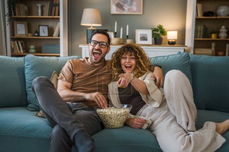 Photo for Couple man and woman caucasian husband and wife or boyfriend and girlfriend sit on the sofa bed at home watch tv movie series with bowl of popcorn happy smile bonding love family concept copy space - Royalty Free Image