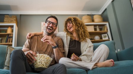 Photo for Couple man and woman caucasian husband and wife or boyfriend and girlfriend sit on the sofa bed at home watch tv movie series with bowl of popcorn happy smile bonding love family concept copy space - Royalty Free Image