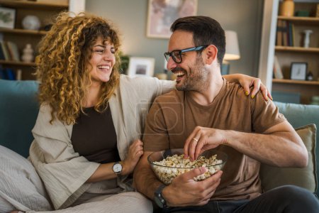 Couple man and woman caucasian husband and wife or boyfriend and girlfriend sit on the sofa bed at home watch tv movie series with bowl of popcorn happy smile bonding love family concept copy space