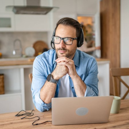 Photo for One man caucasian male freelancer work from home with headphones on his head on laptop computer customer support thinking serious his wife stand in the background - Royalty Free Image