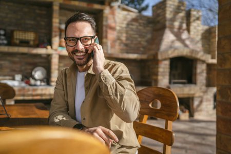 Photo for One man adult caucasian male with beard and eyeglasses outdoor in sunny day happy smile use mobile smart phone to make a call talk copy space real people - Royalty Free Image