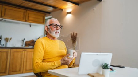 Photo for One senior man sit at home in the kitchen with cup of tea or coffee taking a brake from work or prepare for daily task morning routine real person copy space domestic life active senior - Royalty Free Image