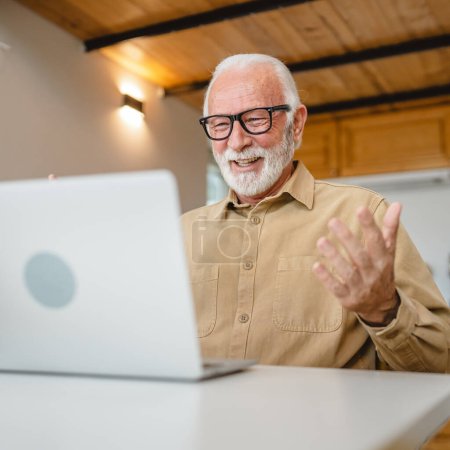 Téléchargez les photos : Un homme caucasien senior grand-père avec barbe et lunettes de travail sur ordinateur portable utiliser ordinateur à la maison en ligne heureux sourire succès - en image libre de droit