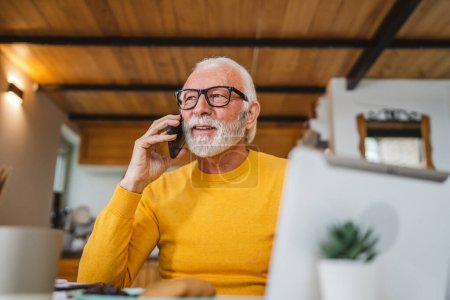 Téléchargez les photos : Un homme caucasien senior homme avec barbe grise assis dans la journée utiliser un téléphone intelligent mobile pour faire un travail d'espace de copie de conversation d'appel de la maison - en image libre de droit