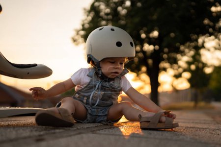Photo for One girl small caucasian toddler child fall of the children's kick scooter wear protective helmet while playing outdoor in summer evening real people leisure growing up concept copy space - Royalty Free Image
