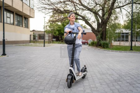 Téléchargez les photos : Une femme mature caucasienne senior debout en plein air avec scooter électrique coup de pied dans la journée confiante femme d'affaires en utilisant un mode de transport alternatif moderne personnes réelles copier l'espace - en image libre de droit