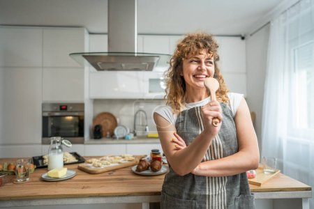 Téléchargez les photos : Une jeune femme caucasienne adulte heureuse porter tablier dans la cuisine sourire tenir mélanger cuillère chanter - en image libre de droit