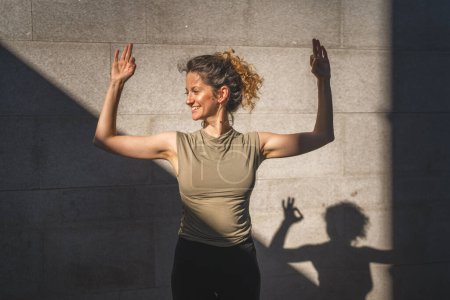 Téléchargez les photos : Une femme caucasienne adulte pratiquant le yoga en plein air jour d'été dans la ville en face du mur avec ombre et soleil mode de vie sain concept de bien-être auto-soin - en image libre de droit
