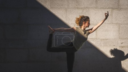 Foto de Una mujer caucásica adulta practicando yoga en el día de verano al aire libre en la ciudad frente a la pared con sombra y sol estilo de vida saludable concepto de bienestar autocuidado - Imagen libre de derechos