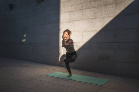 Foto de Una mujer caucásica adulta practicando yoga en el día de verano al aire libre en la ciudad frente a la pared con sombra y sol estilo de vida saludable concepto de bienestar autocuidado - Imagen libre de derechos