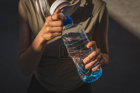 Foto de Primer plano en las manos sección media de mujer caucásica desconocida abierta botella de plástico de agua, mientras que de pie al aire libre en el día soleado - Imagen libre de derechos