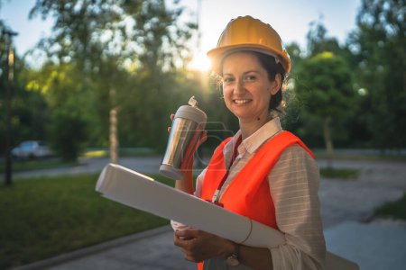 Photo for Architect woman female construction engineer stand outdoors wear protective helmet and west in front of modern building wall hold takeaway coffee - Royalty Free Image