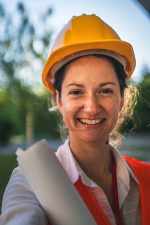 Photo for Architect woman female construction engineer stand outdoors wear protective helmet and west in front of modern building wall self portrait selfie UGC user generated content - Royalty Free Image