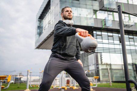 Ein Mann junge kaukasische männliche Sportler stehen im Freien in Tagestraining mit russischer Glocke girya Kettlebell Gewichtsübung echte Person Kopierraum