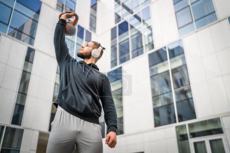Foto de Un hombre joven atleta caucásico pie al aire libre en el entrenamiento de día con campana rusa girya kettlebell peso ejercicio persona real copiar espacio - Imagen libre de derechos